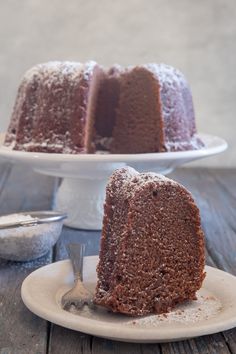 a bundt cake with powdered sugar on top sits on a plate next to a fork