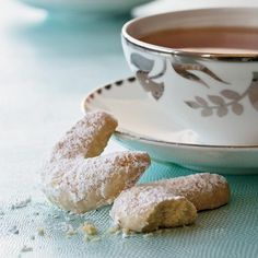 two powdered sugar donuts next to a cup of tea