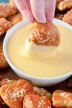 a hand dipping cheese into a bowl of croissants with other pastries in the background