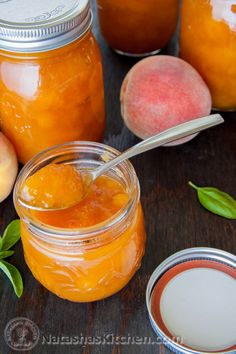 jars filled with peach jam sitting on top of a table next to sliced peaches