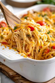 a casserole dish with noodles and vegetables being lifted by a wooden spatula