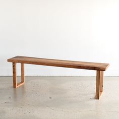 a long wooden bench sitting on top of a cement floor next to a white wall