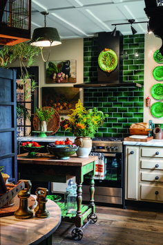 a kitchen with green tiles on the wall and wooden flooring, along with potted plants