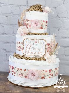 a three tiered cake with pink flowers on the top and baby in bloom written on the bottom