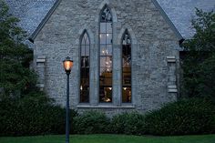 an old stone church with a clock on it's face and windows lit up at night