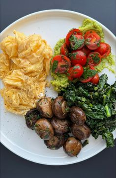 a white plate topped with potatoes, spinach and tomato salad next to other foods