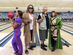 three people in costumes standing on a bowling alley, one holding a red ball and the other looking up