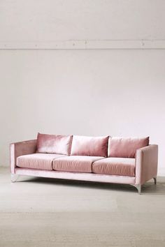 a pink couch sitting in the middle of a room with white walls and flooring