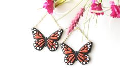 two red and black butterfly shaped earrings on a white surface with flowers in the background