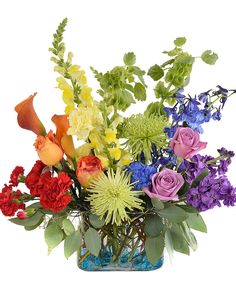 an arrangement of colorful flowers in a blue glass vase on a white background with green leaves