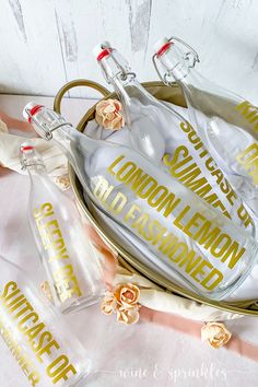 three clear bottles with gold lettering sitting on top of each other next to some pink roses