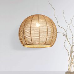 a rattan light hanging over a table next to a vase with branches in it