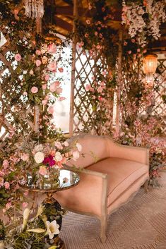 a pink couch sitting next to a glass table with flowers on it and chandelier hanging from the ceiling