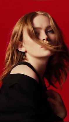 a woman with her hair blowing in the wind and looking at the camera, against a red background