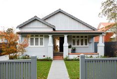 a grey house with white trim on the front door and side porch, fenced in