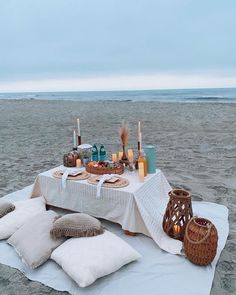 a table set up on the beach with candles and food