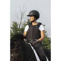 a woman riding on the back of a black horse wearing a helmet and safety gear