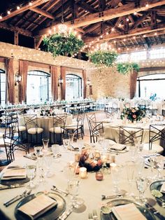 the tables are set for an event with white linens and greenery hanging from the ceiling