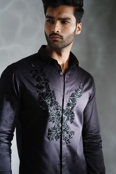 a young man wearing a black shirt with an intricate design on the chest and sleeves