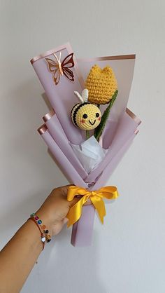 a hand is holding a bouquet made out of crochet and paper with a stuffed animal on it