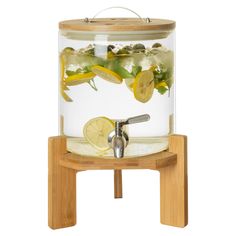 a glass jar filled with lemons and water on top of a wooden stand next to a white wall