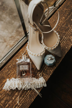 a pair of white high heeled shoes next to a perfume bottle on a wooden table