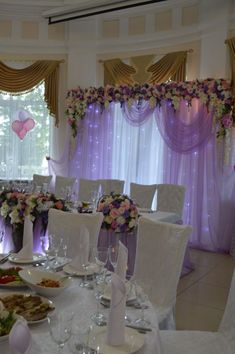 a banquet room with white chairs and purple drapes on the windows, decorated with flowers