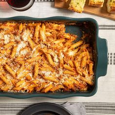 a casserole dish with pasta and parmesan cheese on the side next to bread