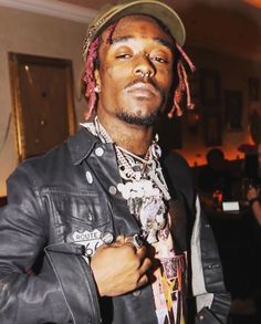 a man with dreadlocks wearing a hat and leather jacket standing in a room