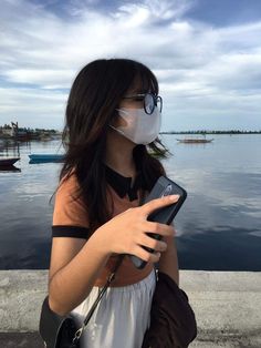 a woman wearing a face mask and holding a cell phone in front of the water