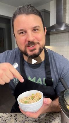 a man in an apron is holding a bowl of food and pointing to the camera