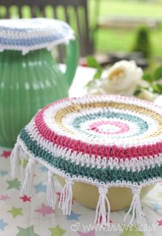 a crocheted dishcloth with tassels sits on a table next to a green vase