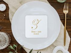 a white plate topped with a square coaster on top of a wooden table next to utensils