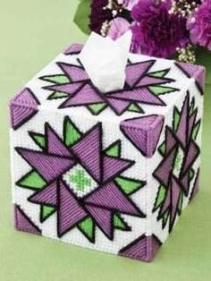 a tissue box decorated with purple and green geometric designs, next to flowers on a table