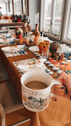 a person holding a cup of coffee in front of a table with plates and napkins