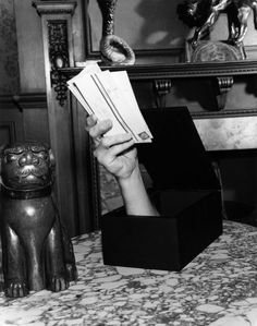 a black and white photo of a person's hand holding up some paper in front of a cat figurine