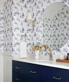 a bathroom with blue and white wallpaper has a large round mirror on the vanity