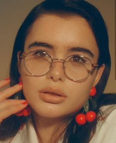 a woman wearing glasses with red beads on her fingers and holding her hand up to her face