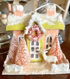 a small house with snow on the roof and trees around it, sitting on a table