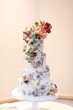 a wedding cake decorated with flowers on a white pedestal in front of a pink wall