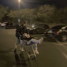 a man pushing a young boy in a shopping cart down the street at night time