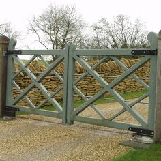 an open gate on the side of a road with grass and trees in the background