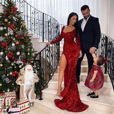 a man and woman in red dress standing on stairs next to a christmas tree with presents