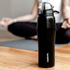 a woman sitting on the floor in front of a black water bottle and yoga mat