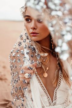 a woman wearing a veil and jewelry standing in the sand with her hands on her hips