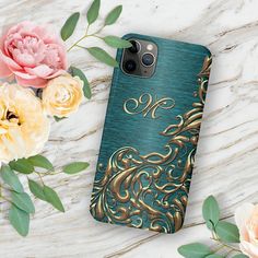 a phone case with gold and blue designs on it next to some flowers, leaves and peonies