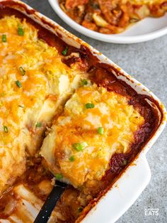 a casserole dish with meat and cheese in it on a table next to two plates