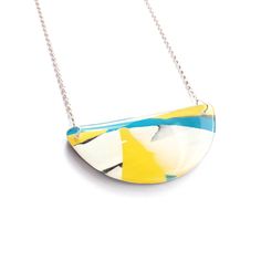 a white and blue necklace with a yellow triangle design on it's end hanging from a silver chain