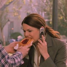 a man and woman eating hotdogs while talking on their cell phones