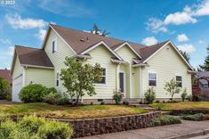 a yellow house with trees and bushes in front